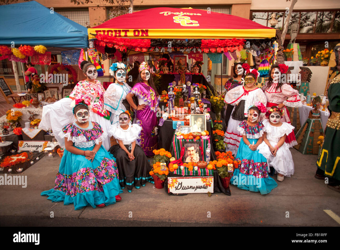 Wearing makeup resembling the  face of La Calavera Catrina ('Dapper Skeleton') family members pose at an altar honoring a deceased relative during the Day of the Dead or Dia de Muertos holiday among Hispanics in Santa Ana, CA. The holiday focuses on gathe Stock Photo
