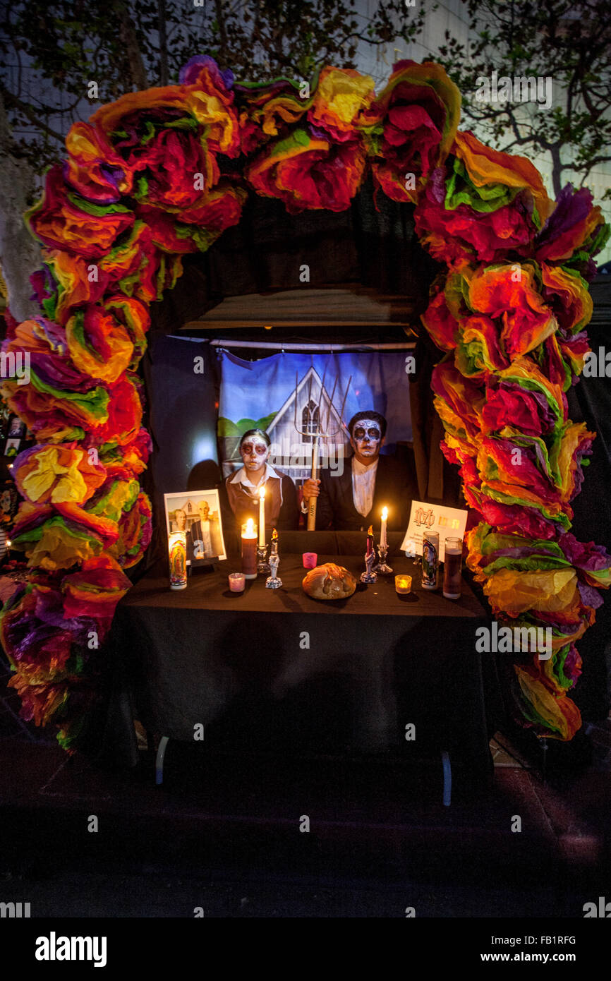 Wearing makeup resembling the  face of La Calavera Catrina ('Dapper Skeleton') juxtaposed with the famous Grant Wood painting 'American Gothic' a couple pose at an altar honoring a deceased relative during the Day of the Dead or Dia de Muertos holiday amo Stock Photo