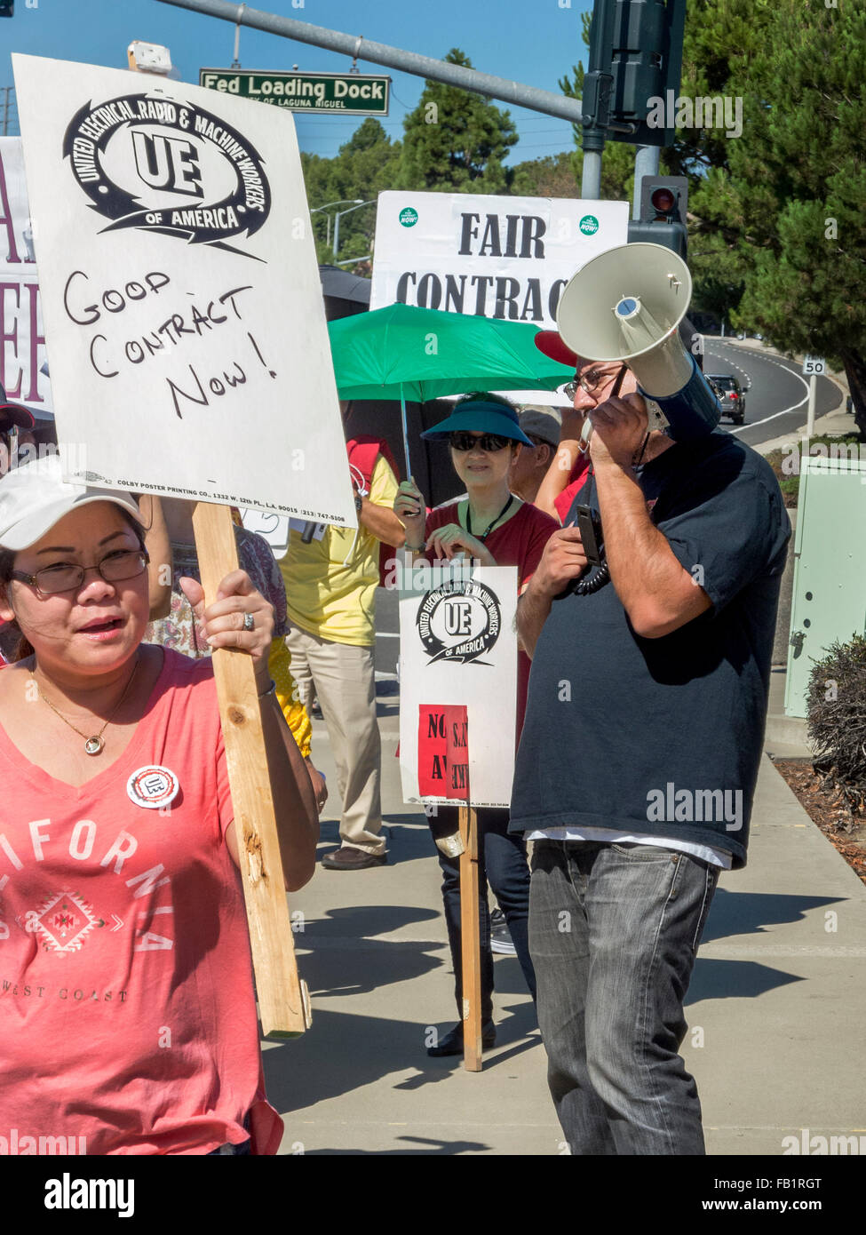 Multiracial striking electrical union workers picket a US Government building in Laguna Niguel, CA, protesting lack of scheduled salary increases. Note federal loading dock sign in background and organizer will bull horn. Stock Photo