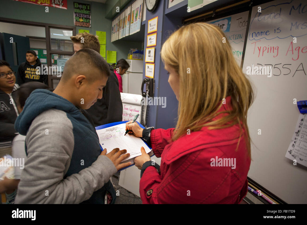 A San Clemente, CA, middle school teacher signs a male teenage student's attendance sheet. Stock Photo