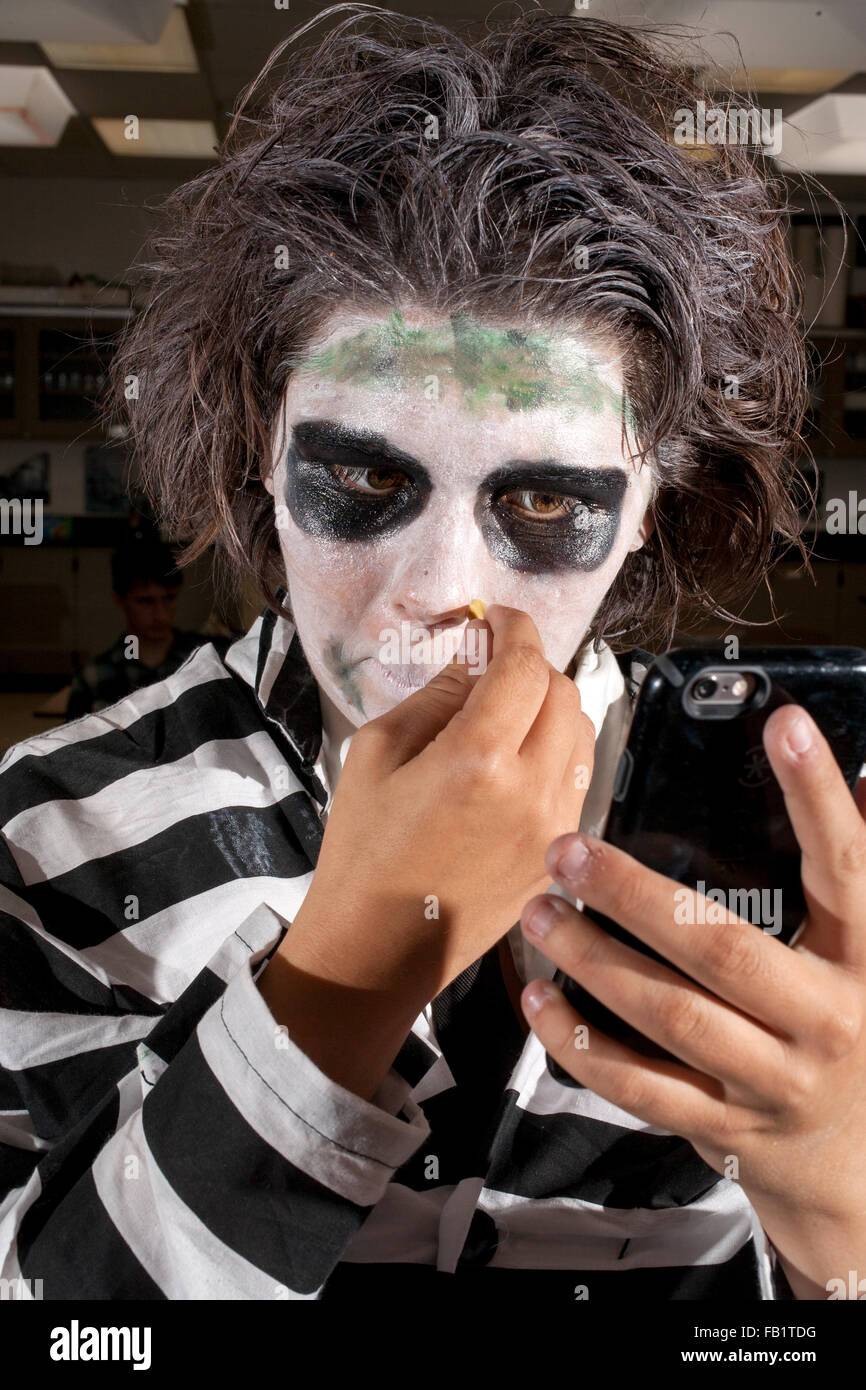 Using a cell phone camera as a mirror, a San Clemente, CA, high school girl puts on grotesque makeup for Halloween. Note striped costume. Stock Photo