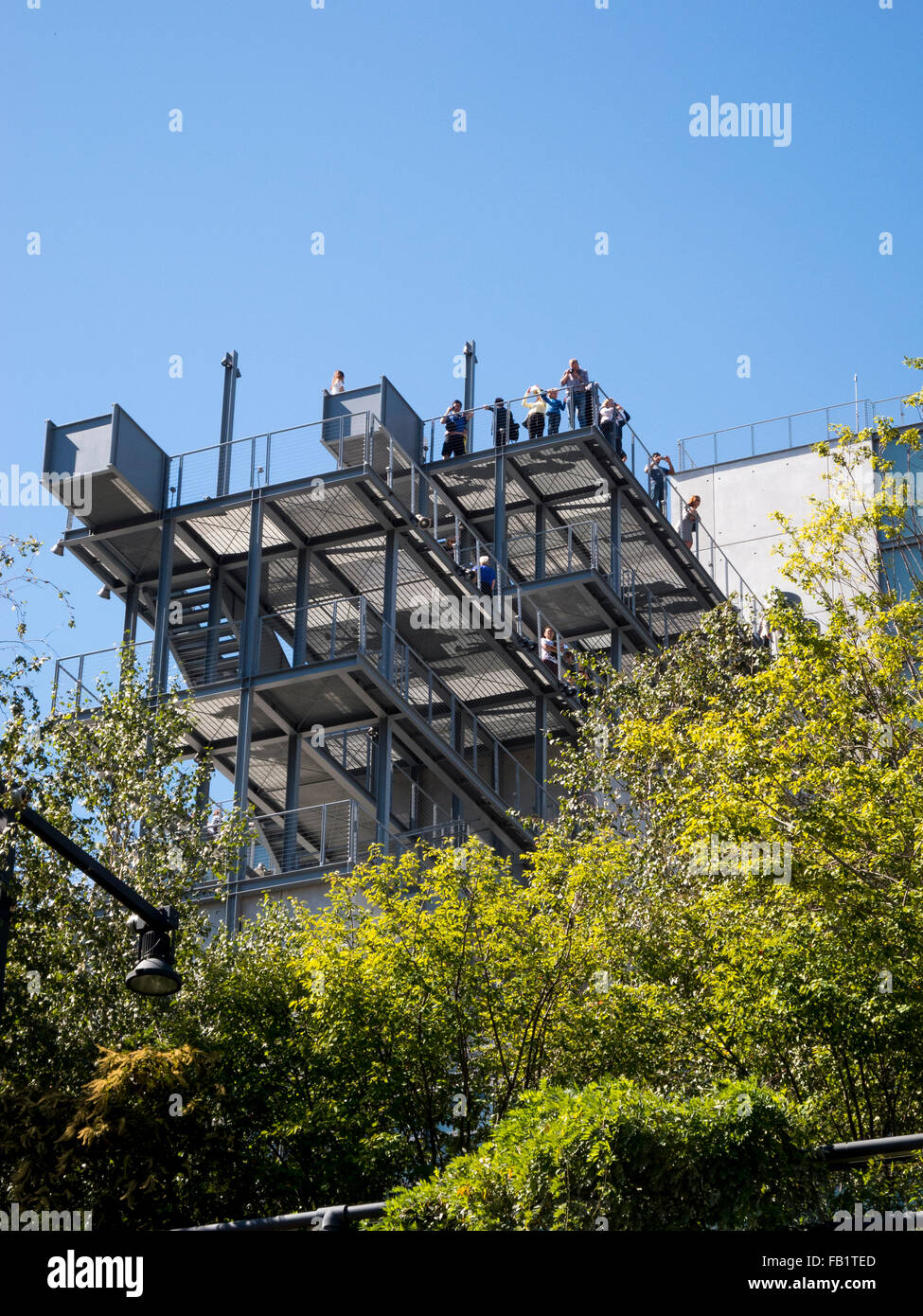 Framed by ornamental trees, visitors to the Whitney Museum of Art in the Meatpacking District of the Lower West Side of Manhattan, New York City, stand on the museum's cantilevered balcony. The museum was designed by architect Renzo Piano. Stock Photo