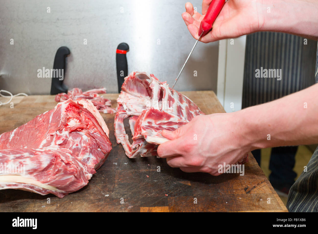 Butcher cutting meat up on a butchers board showing hands and knife. Stock Photo