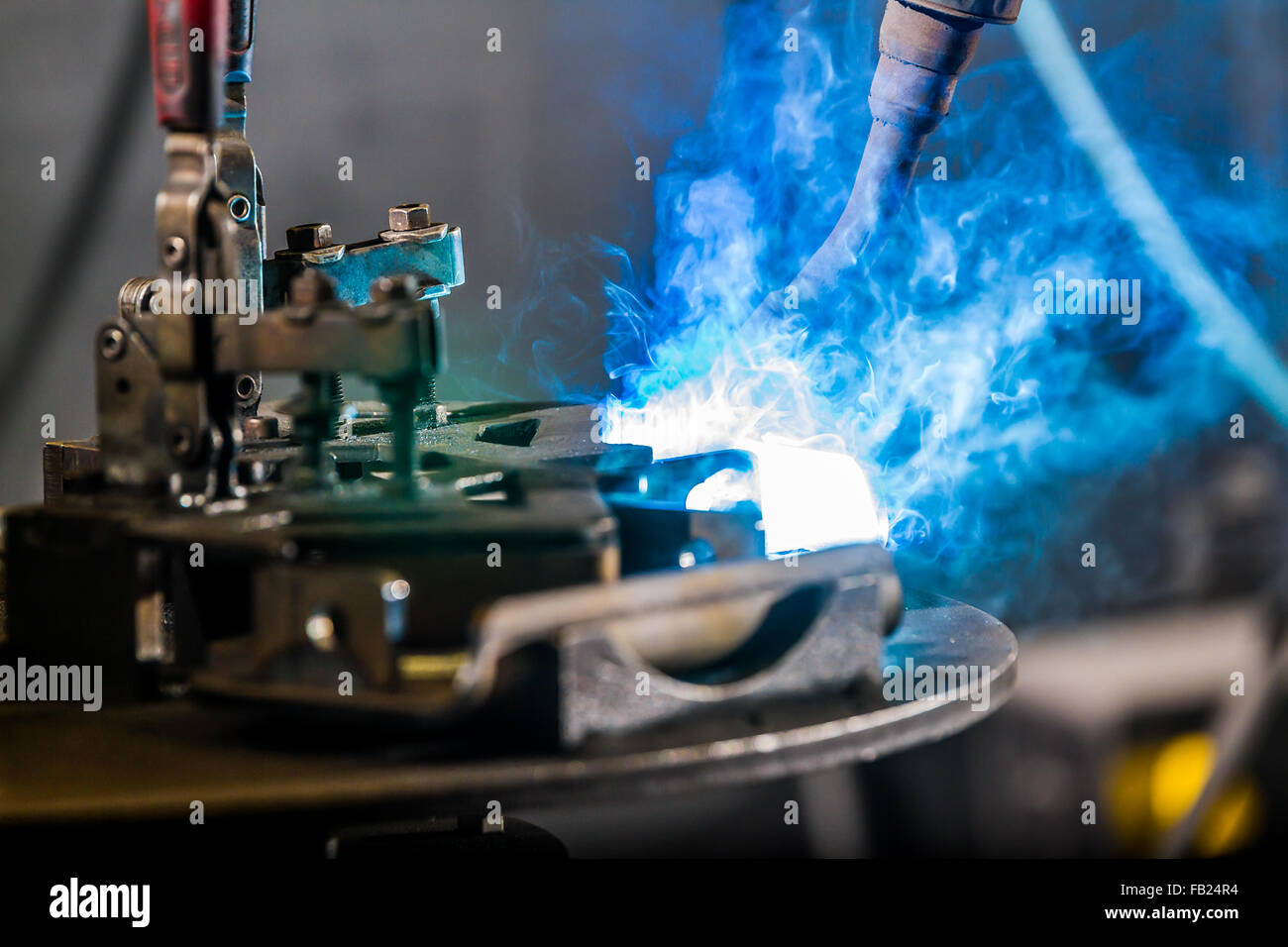 Bright light and smoke from CNC robotic mig welding of half inch steel parts with hold-down clamp and bolts on work table Stock Photo