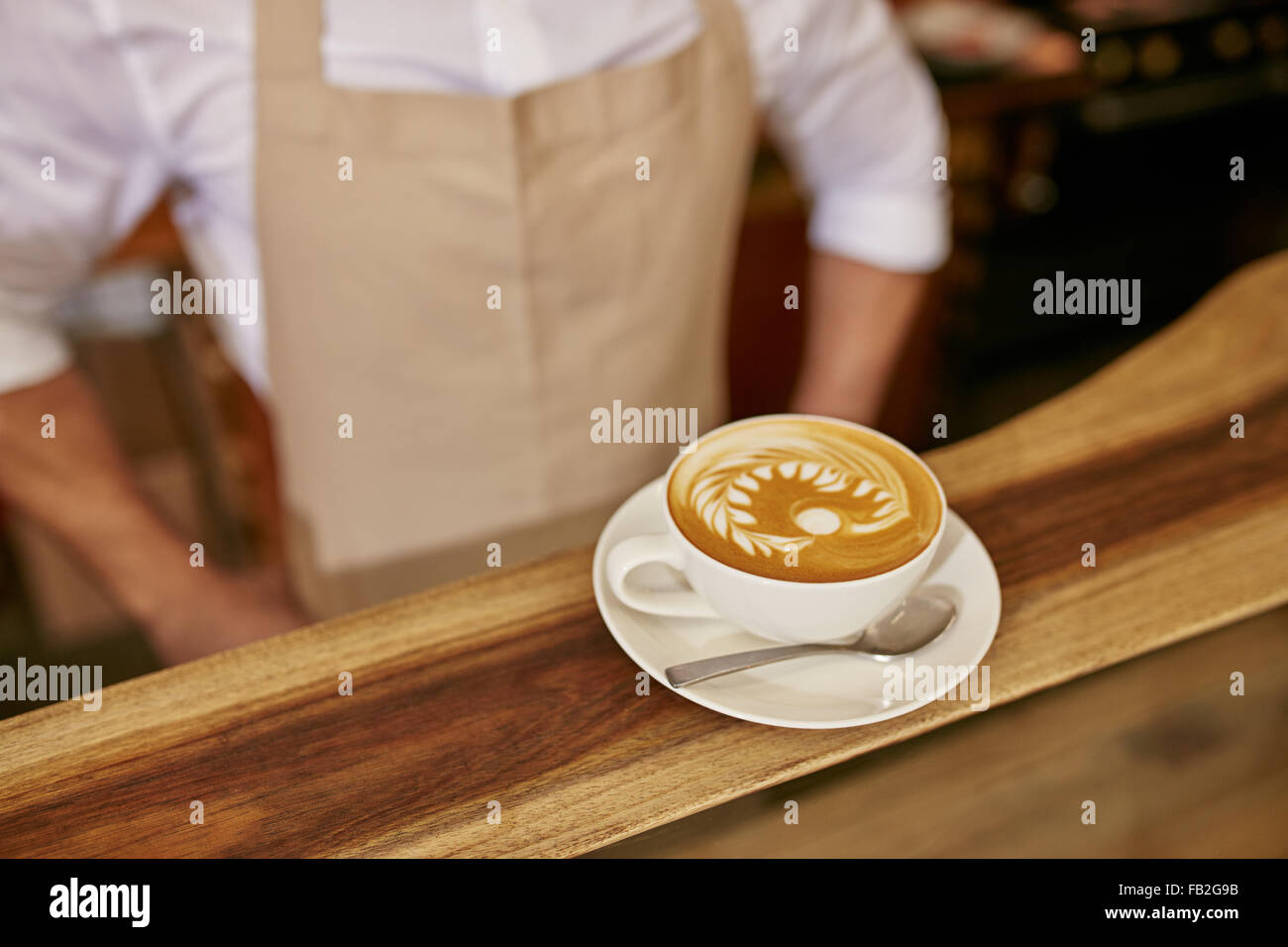 Close up of cup of fresh coffee on the wooden counter with a barista standing by Stock Photo