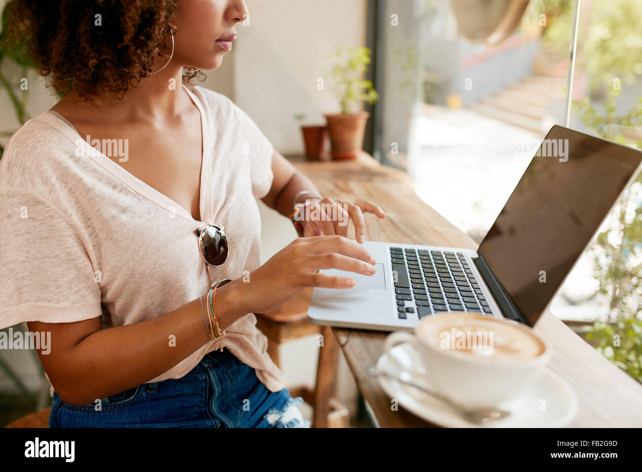 Cropped image of young woman working on laptop while sitting in cafe. African girl using laptop computer with a cup of coffee on Stock Photo