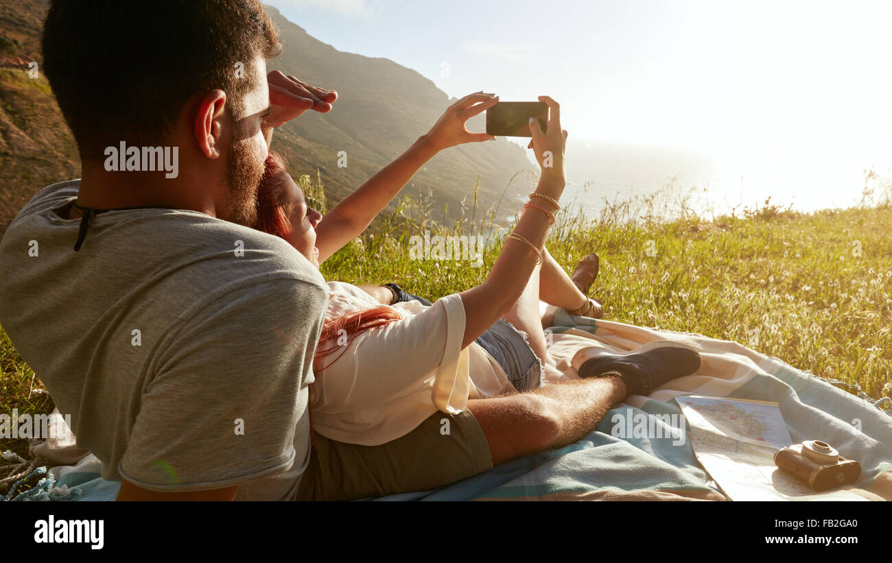 Rear view of young couple on picnic taking a self portrait with their smart phone. Stock Photo