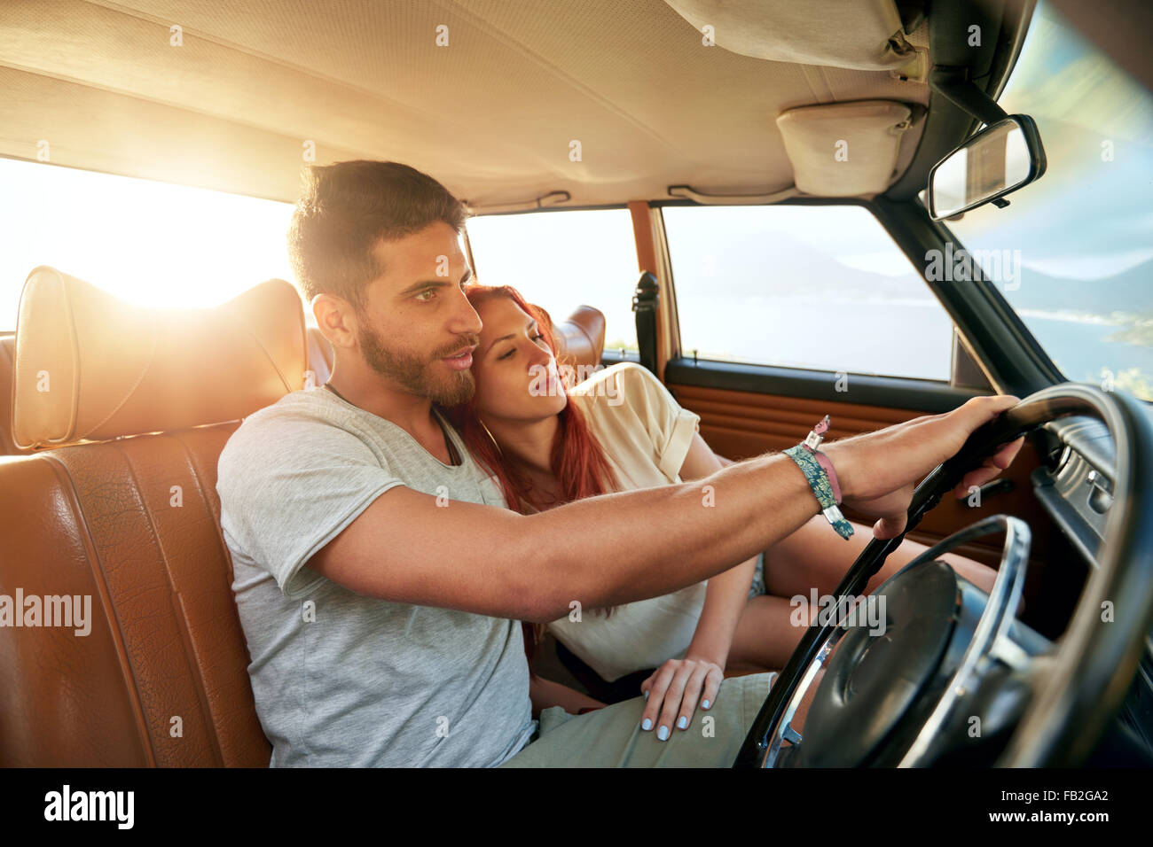 Romantic young couple in their car going on a road trip. Young man driving car with woman sitting by on a summer day. Stock Photo
