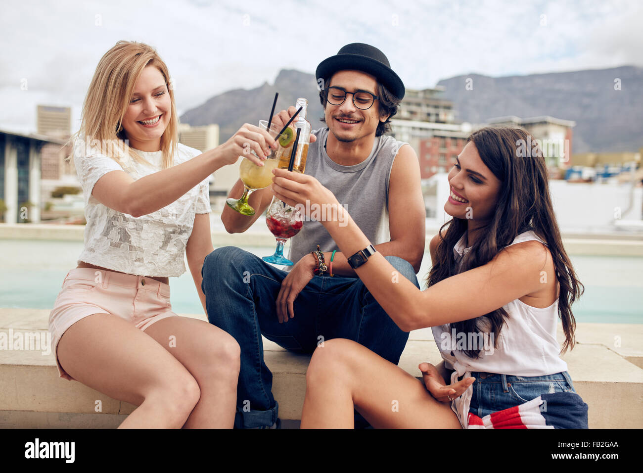 Happy young friends toasting cocktails at a rooftop party. Young people hanging out and enjoying drinks. Stock Photo