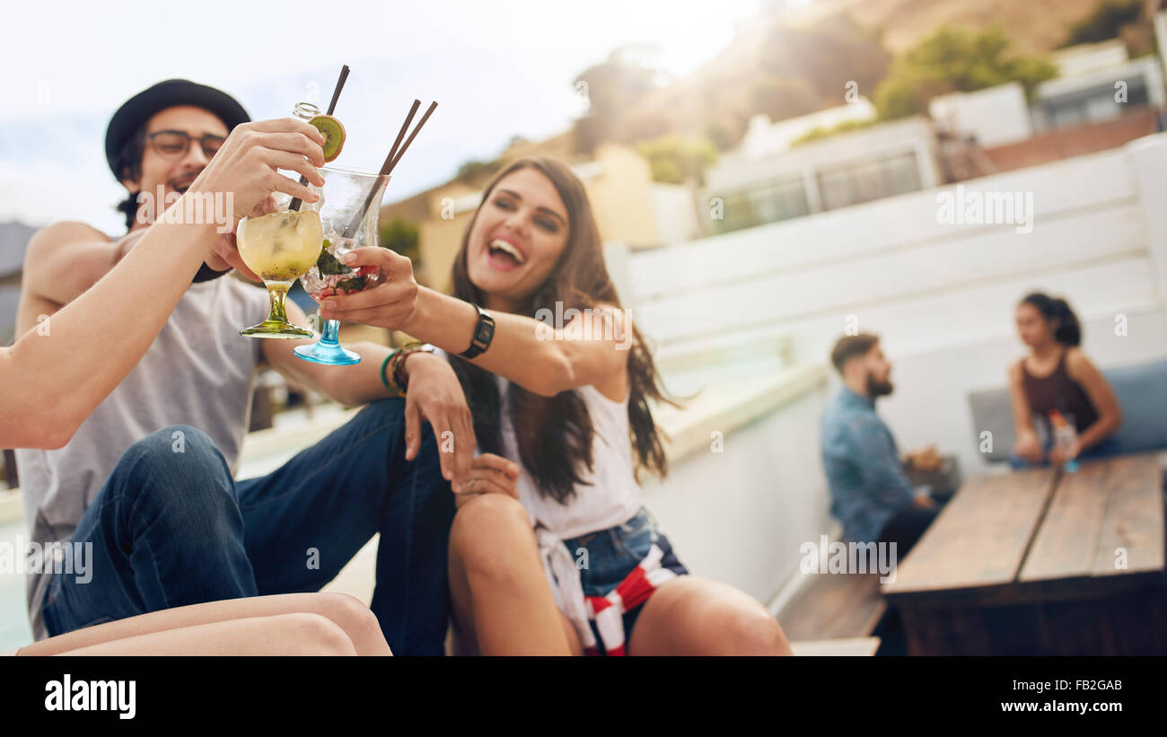 Happy young people toasting cocktails at a rooftop party. Young friends hanging out and enjoying drinks. Stock Photo