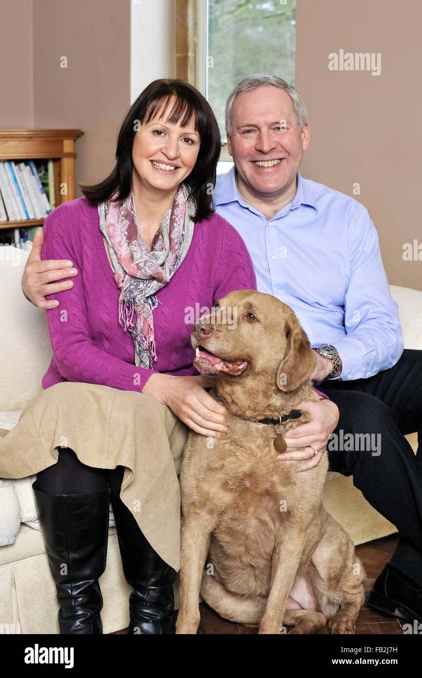 A middle age couple sat on a sofa hugging their dog Stock Photo