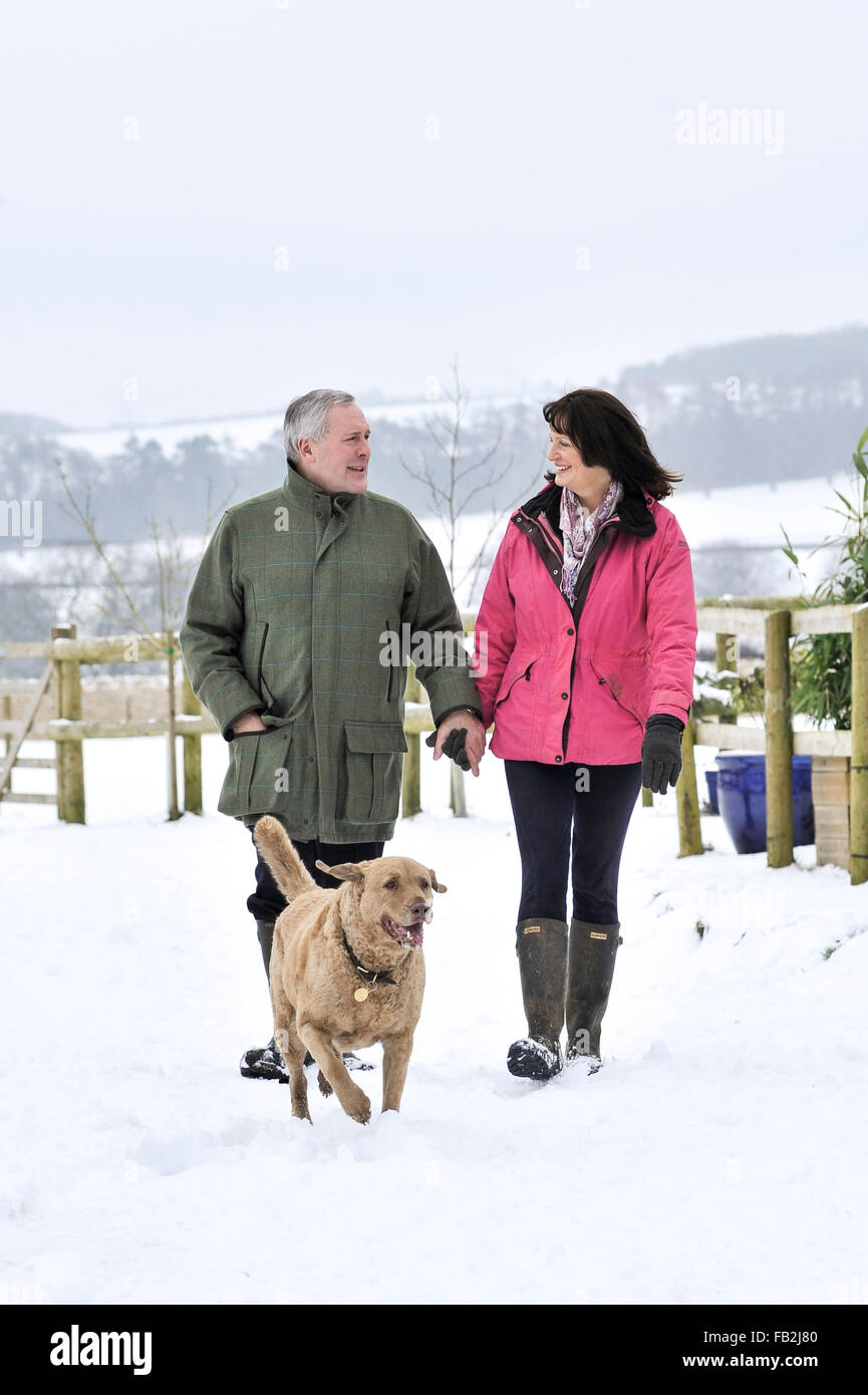Middle aged couple walking their dog in a winter countryside Stock Photo