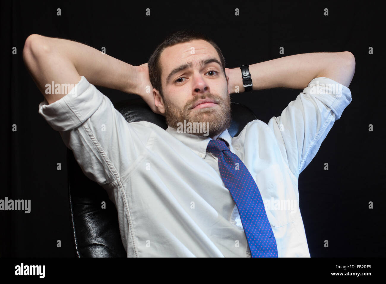 An office worker, wearing a shirt and tie, relaxes in a chair. Stock Photo