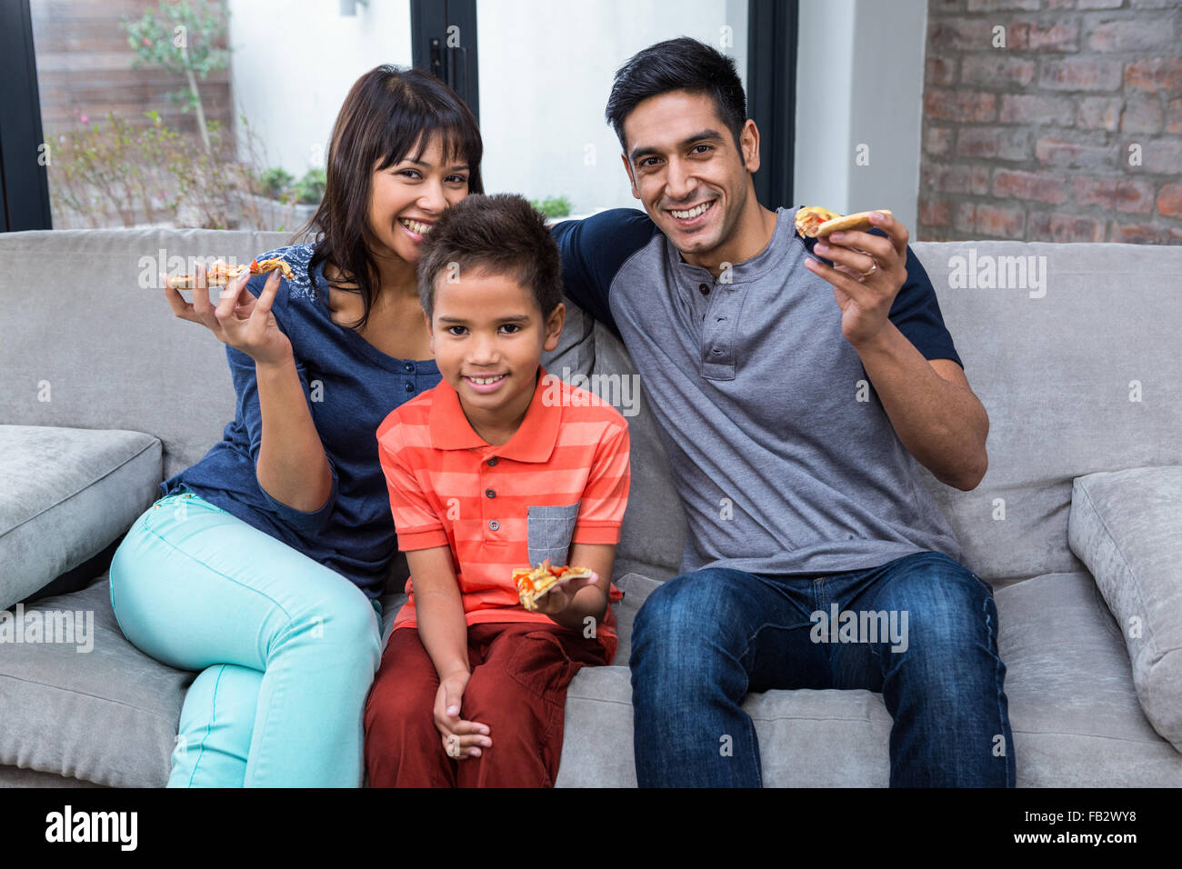 Smiling family eating pizza on the sofa Stock Photo