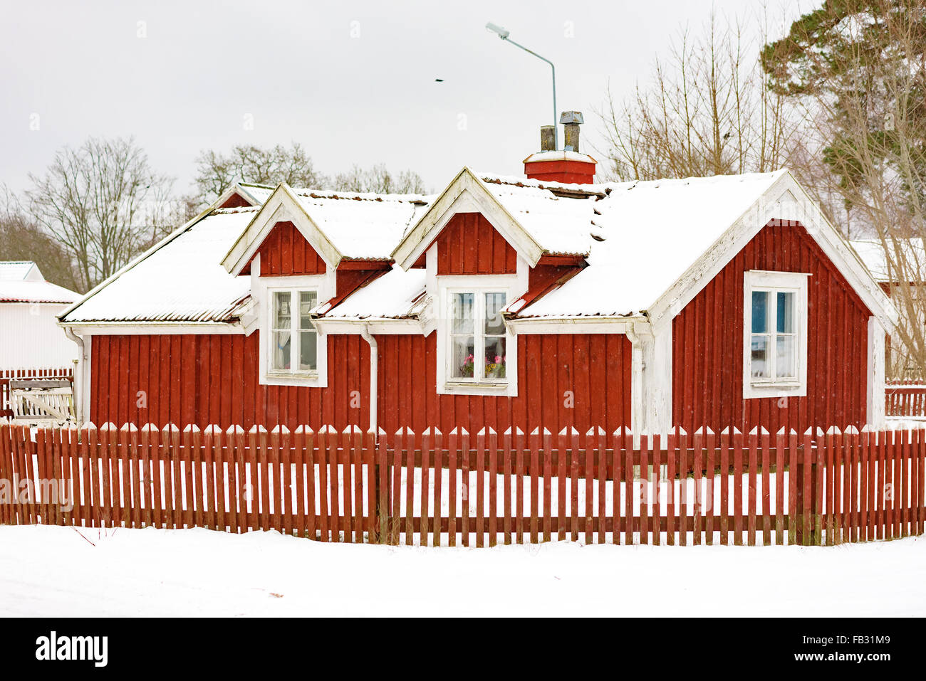 Johannishus, Sweden - January 8, 2016: A small red wooden house with fence and snow covered roof. These kind of houses are often Stock Photo