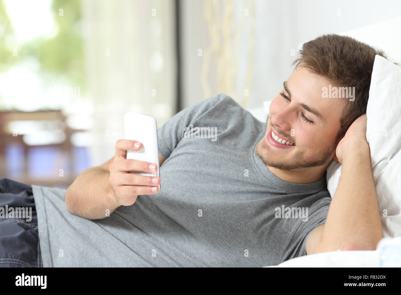 Relaxed casual man using a smart phone lying on the bed at home Stock Photo