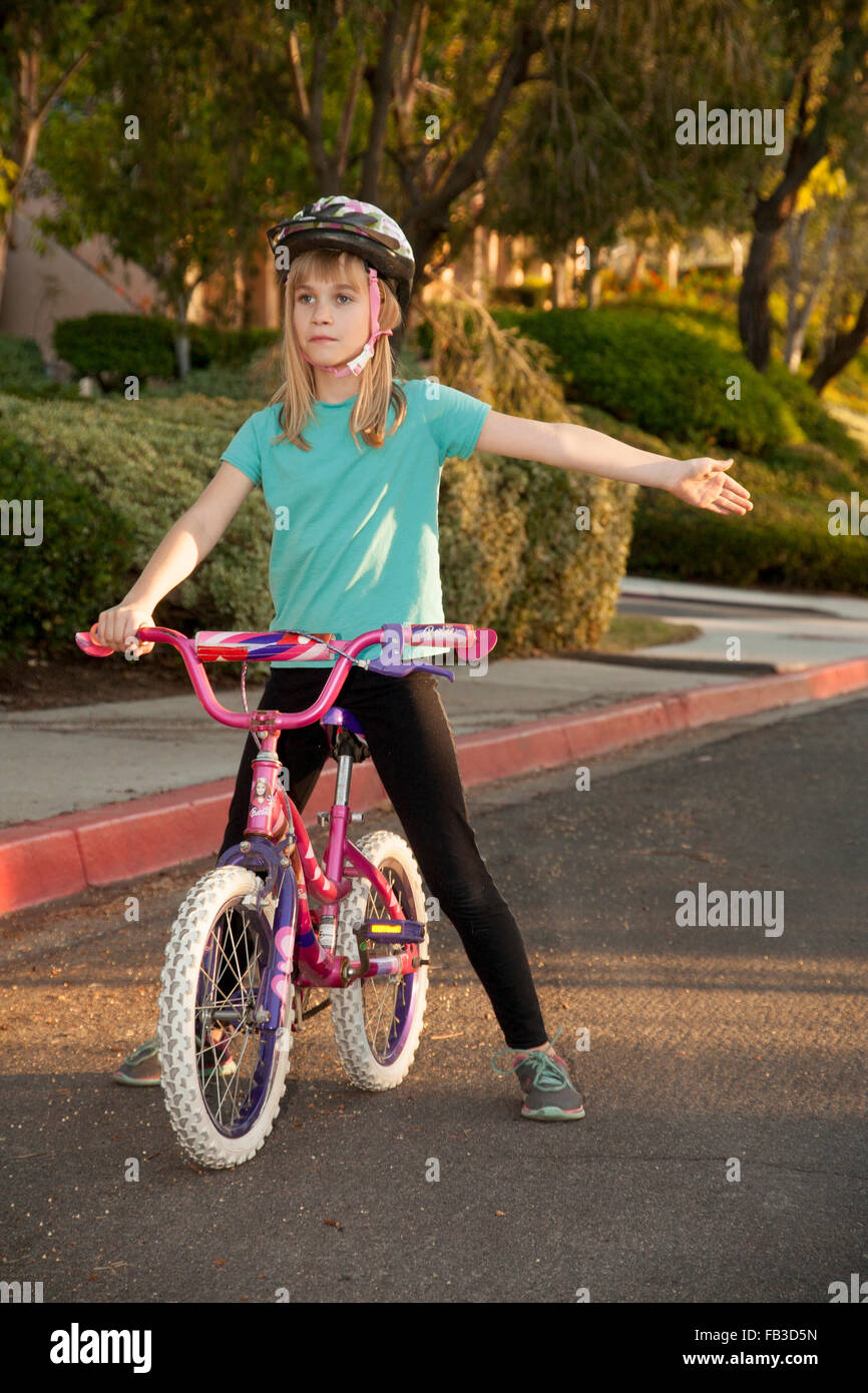 A tween girl bicyclist signals a left turn using her arm on a street in Lake Forest, CA MODEL RELEASE Stock Photo