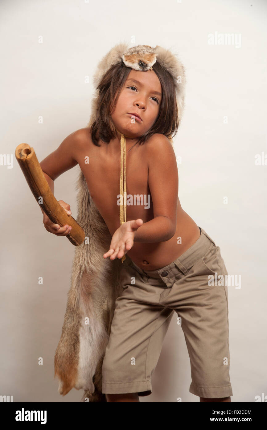 A Native American boy member of the Acjachemen tribe plays the clapper stick, a primitive percussion musical instrument. Note coyote head costume appropriate for male tribal members. MODEL RELEASE MODEL RELEASE Stock Photo