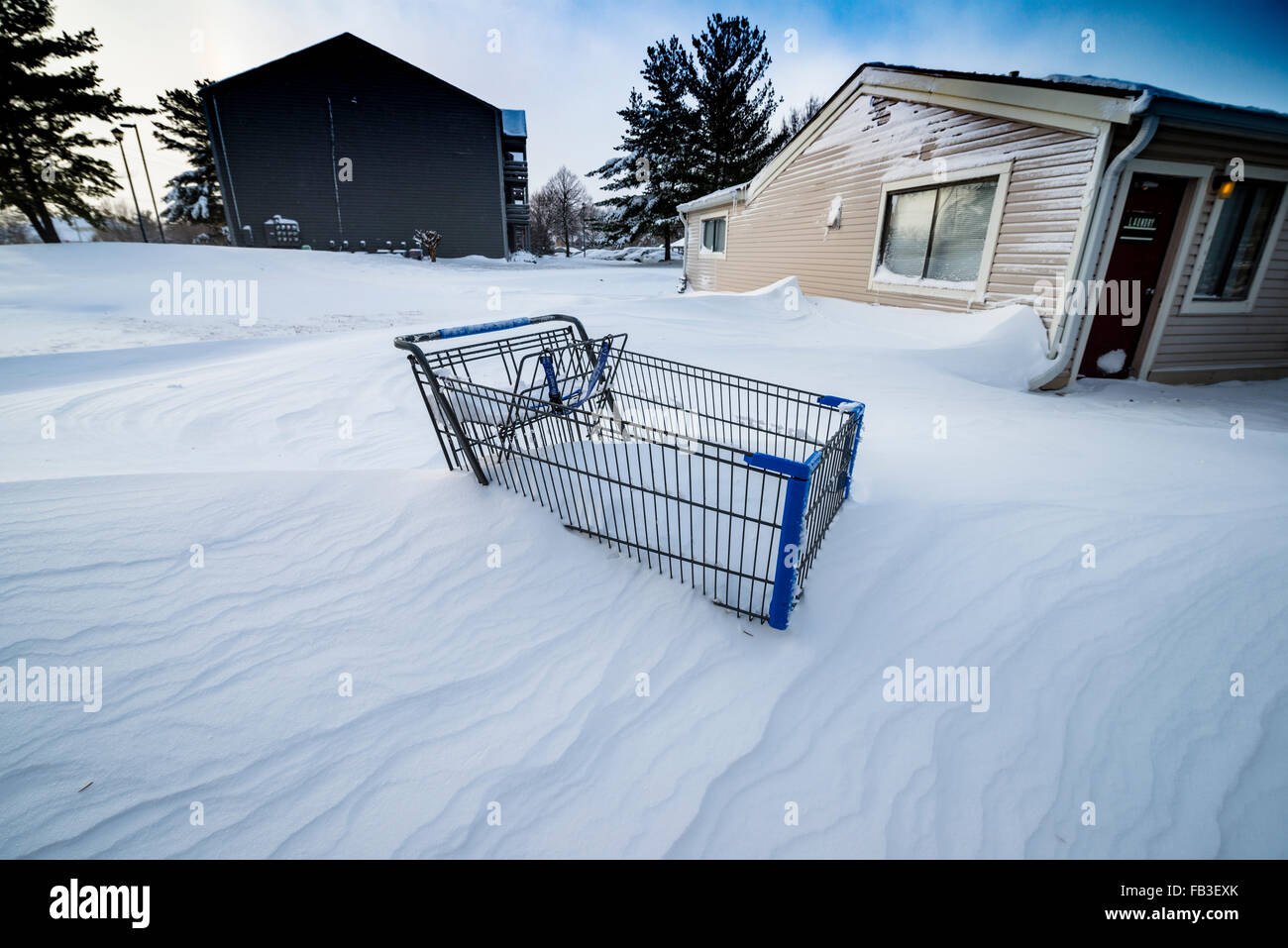 Snow drifted halfway up an abandoned shopping cart near an apartment