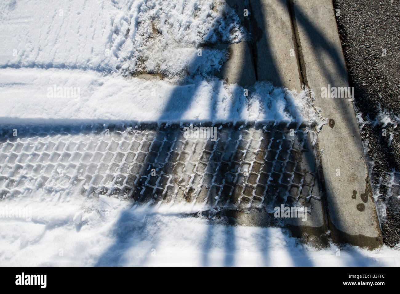 Tire tread in snow on sidewalk leading to street Stock Photo