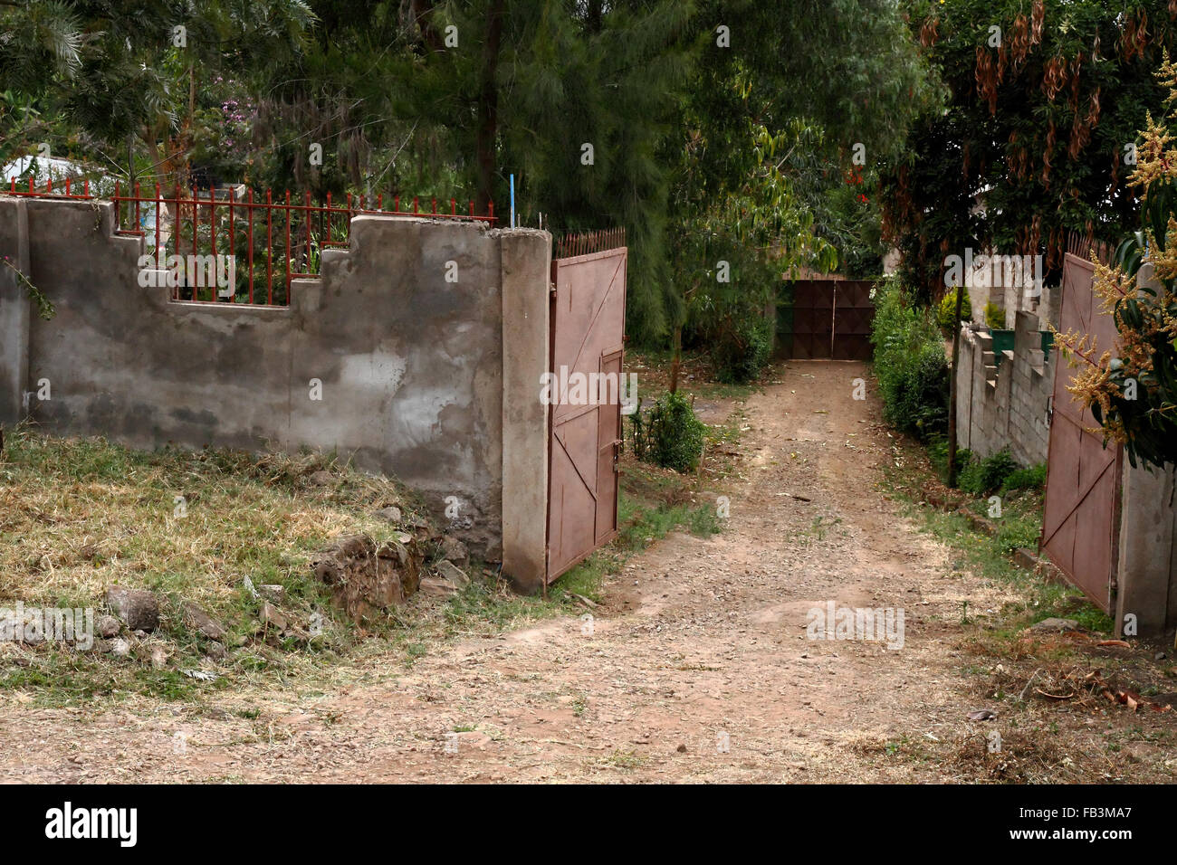 Looking down a path through a walled compound with two solid metal gates Stock Photo