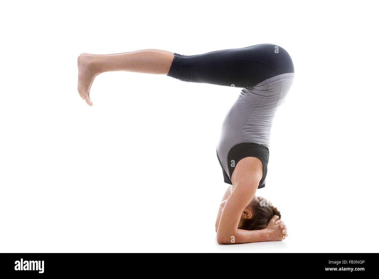 Sporty yoga girl on white background doing a handstand in pose shirshasana (Sirshasana) with bent legs Stock Photo