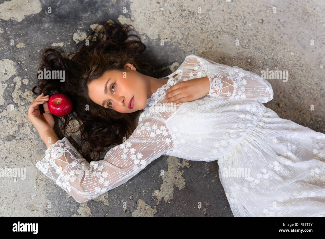 Stunning young woman in white lace dress lying on the floor with a red apple Stock Photo