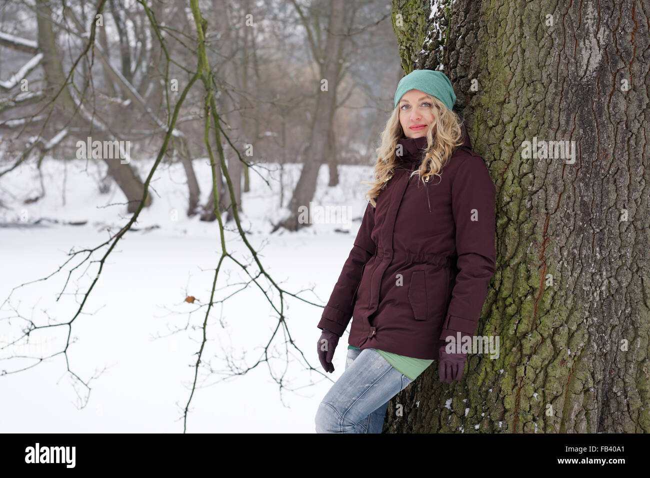 woman leaning against tree in winter landscape Stock Photo