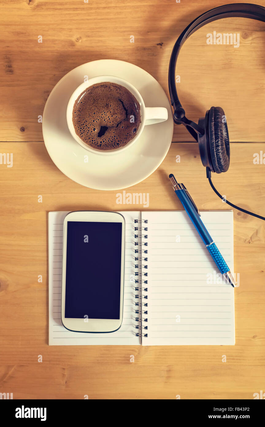 Notebook with pencil, coffee cup,  blank screen smart phone and headphones on wooden table, business concept. Selective focus. Stock Photo