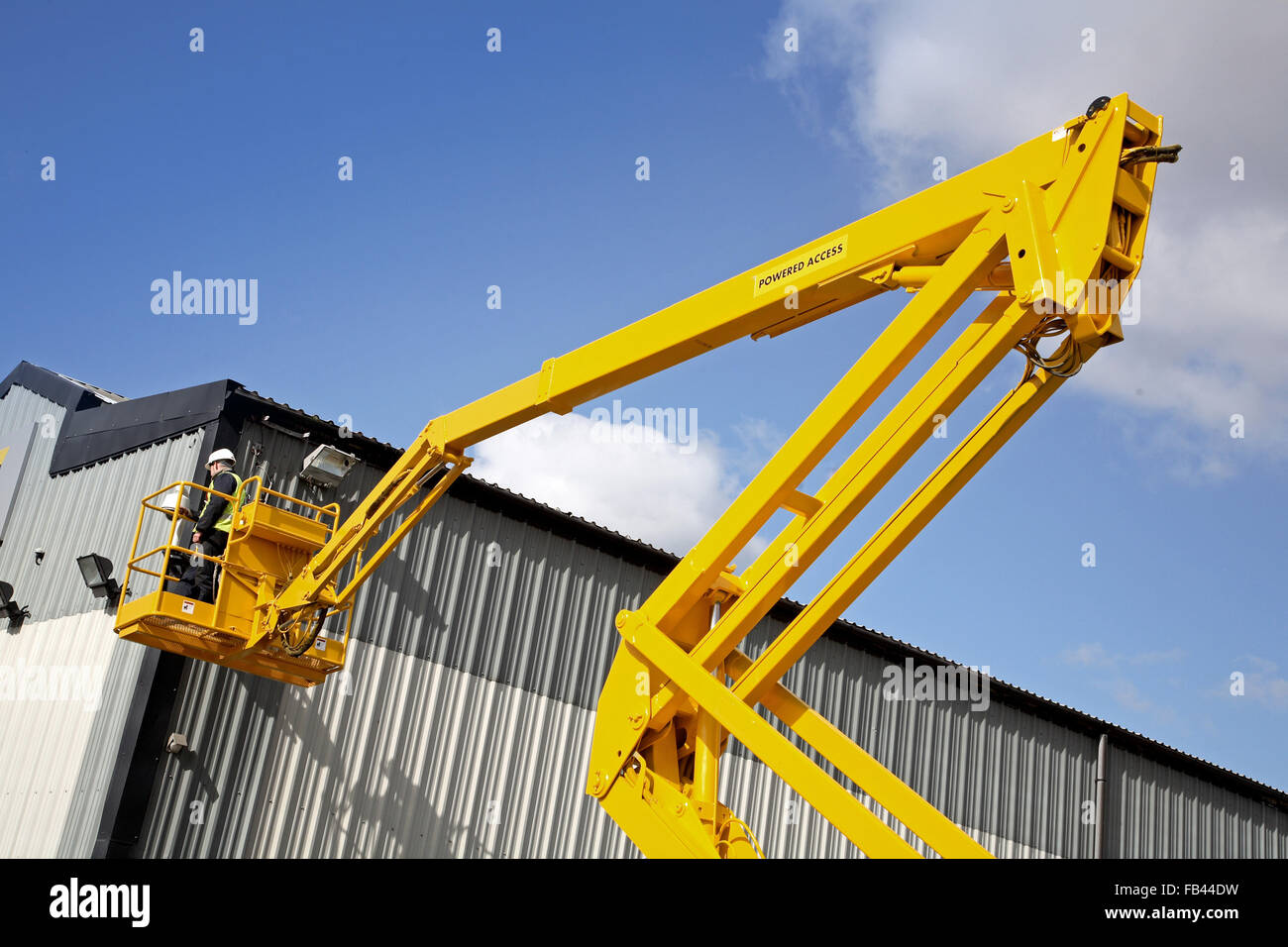 A hydraulic, powered access machine is used to access the exterior of a warehouse building Stock Photo