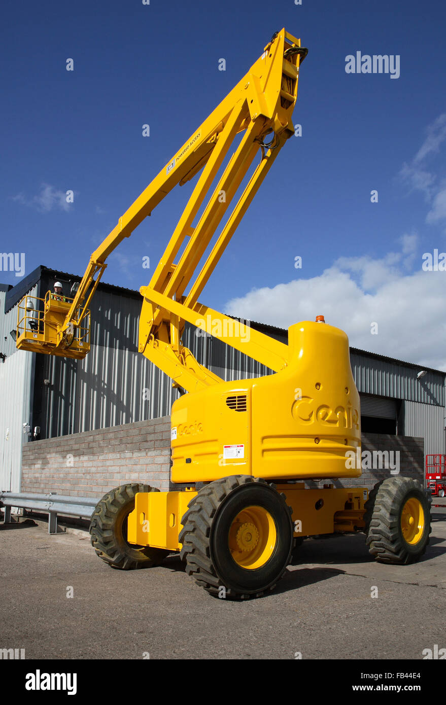 A Genie, diesel-powered, hydraulic access platform is used to access the exterior of a warehouse building Stock Photo