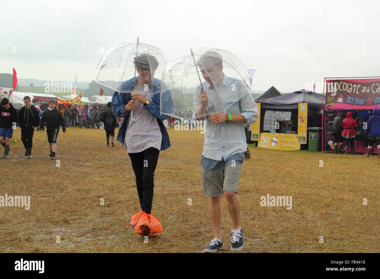 A pair of young men take cover under umbrellas during heavy rainfall at the Y Not music festival, Derbyshire England - August Stock Photo