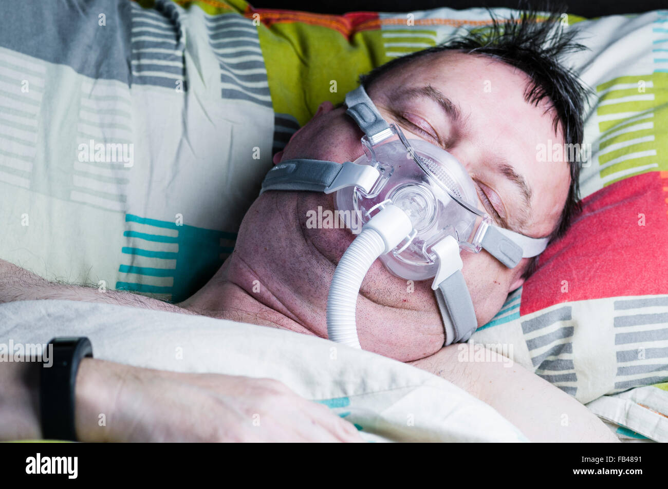 A middle-aged, overweight man wearing a CPAP mask while sleeping in bed Stock Photo