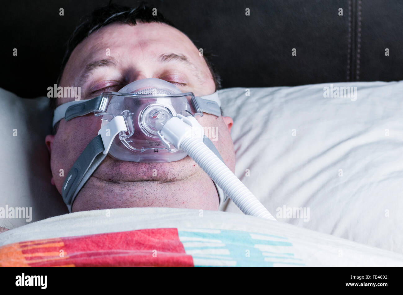 A middle-aged, overweight man wearing a CPAP mask while sleeping in bed Stock Photo