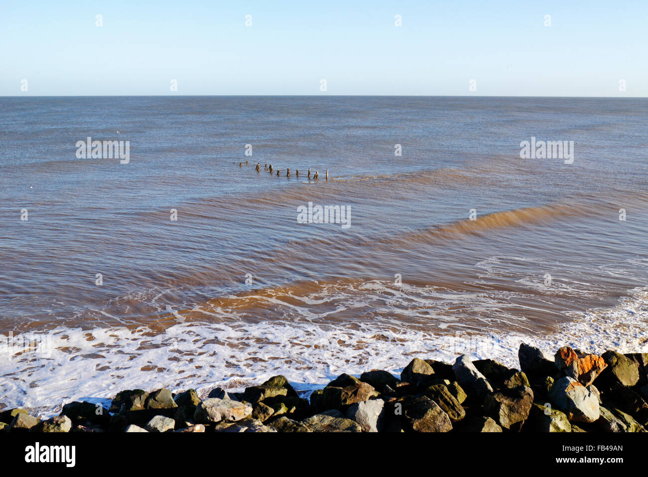A view of rock armour sea defences with old groyne posts showing offshore at Happisburgh, Norfolk, England, United Kingdom. Stock Photo
