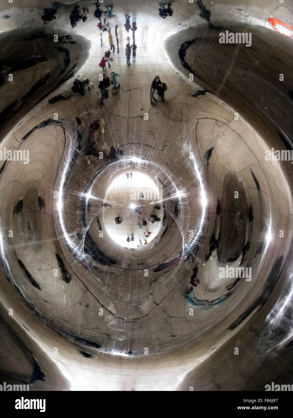 Distorted reflections are seen of sightseers looking underneath at 'The Bean,' the popular nickname for 'Cloud Gate,' a 110-ton elliptical sculpture in Millennium Park in Chicago, Illinois, USA. British artist Anish Kapoor created the shiny monument with pieces of stainless steel that were welded together and then highly polished to visually eliminate all the seams. The artwork took two years to complete and was unveiled in 2006. It has since become one of the major tourist attractions in the Windy City. Stock Photo