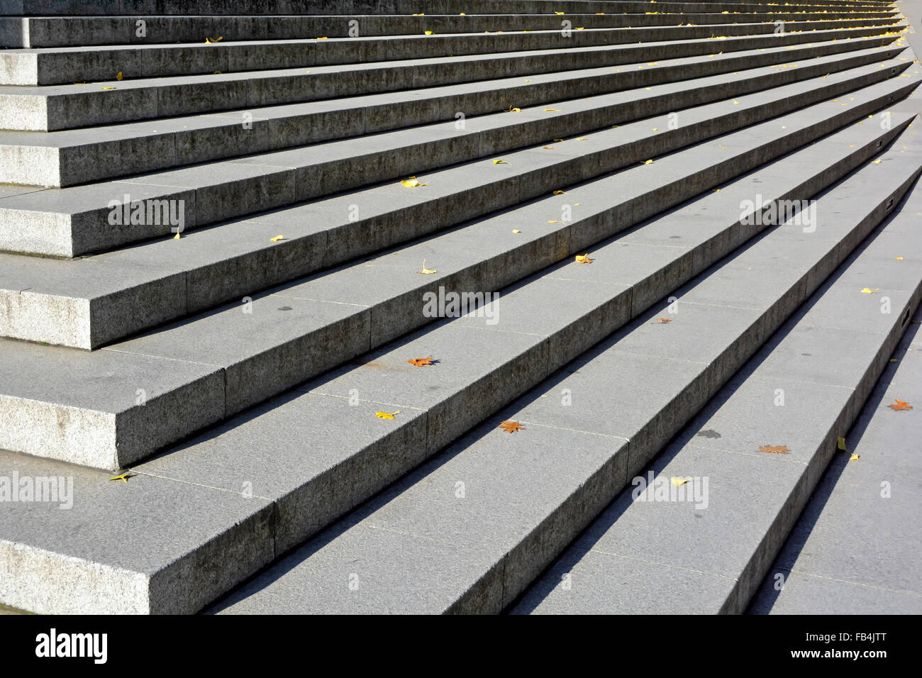 Long straight line of wide stone treads in sunshine and risers in shadow on steps in the City of London sprinkled with fallen autumn leaves England UK Stock Photo