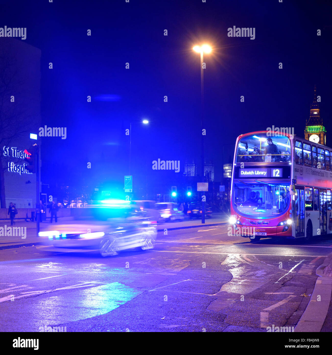 Metropolitan police car with blue flashing lights illuminating night sky on Westminster Bridge with london bus waiting at red traffic light England UK Stock Photo