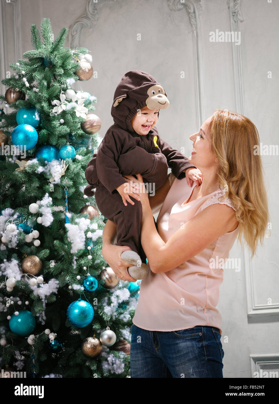 Young woman playing with little son dressed in monkey costume beside Christmas tree Stock Photo