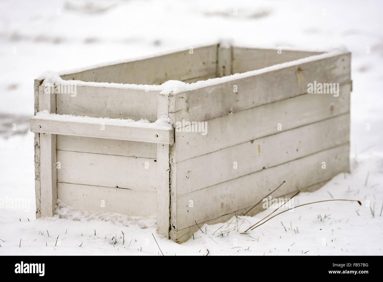 A white open wooden box standing in the snow. Shallow focus on front corner. Stock Photo