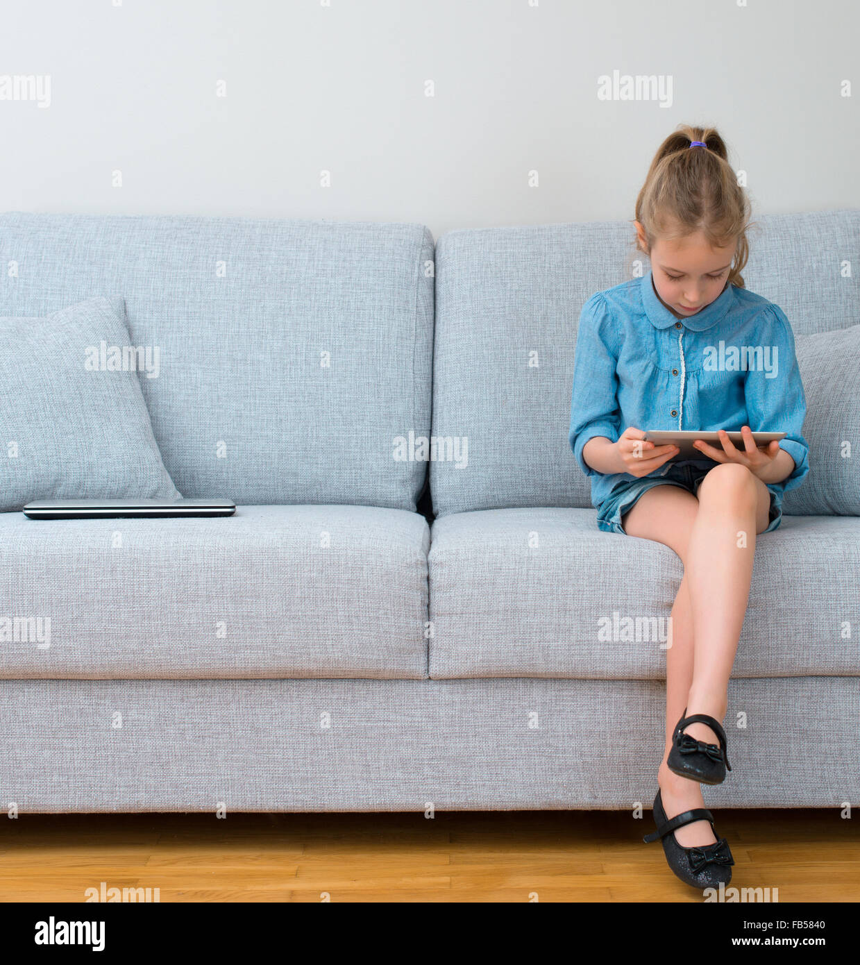 Little girl sitting on sofa and using tablet pc Stock Photo - Alamy