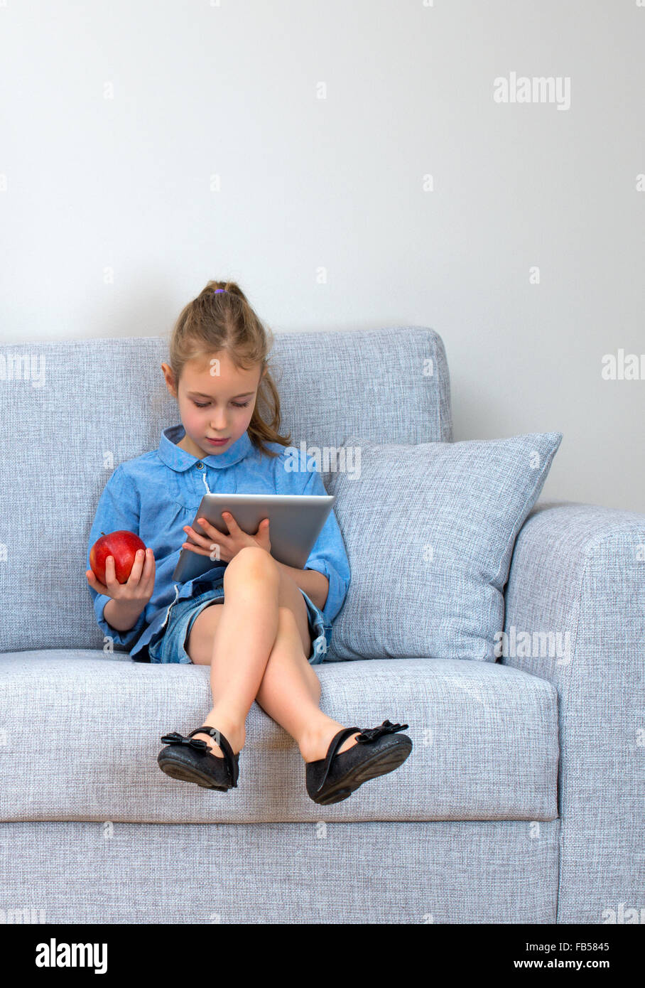 Little girl sitting on sofa and using tablet pc Stock Photo - Alamy