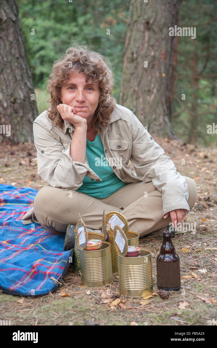 Middle-aged woman sitting on a blanket in front of an open metal cans Stock Photo