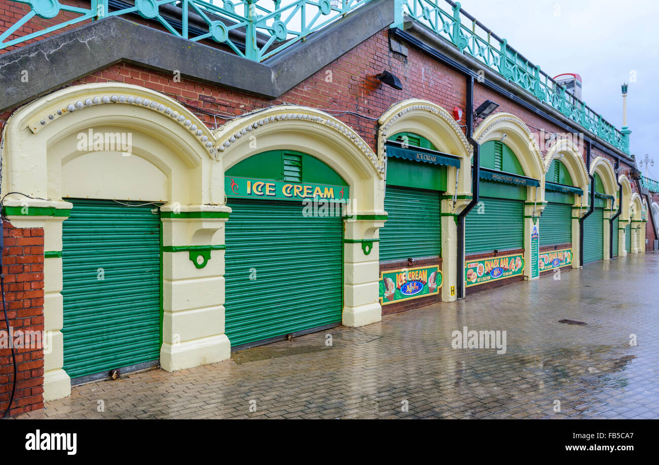 Closed seafront shops with shutters down on a wet day in Winter in Brighton in East Sussex, England, UK. Stock Photo