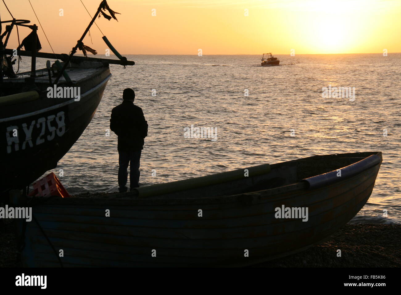 Sunrise in the popular town of Hastings shows the fishing beach at sunrise with a boat coming to shore and two other boats and a Stock Photo