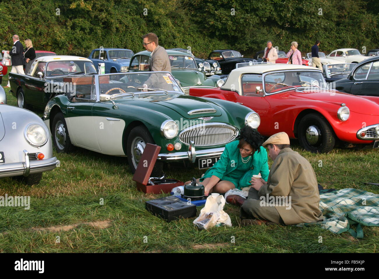 A MAN AND WOMAN IN VINTAGE FASHIONS HAVING A PICNIC AT GOODWOOD REVIVAL SURROUNDED BY CLASSIC CARS Stock Photo