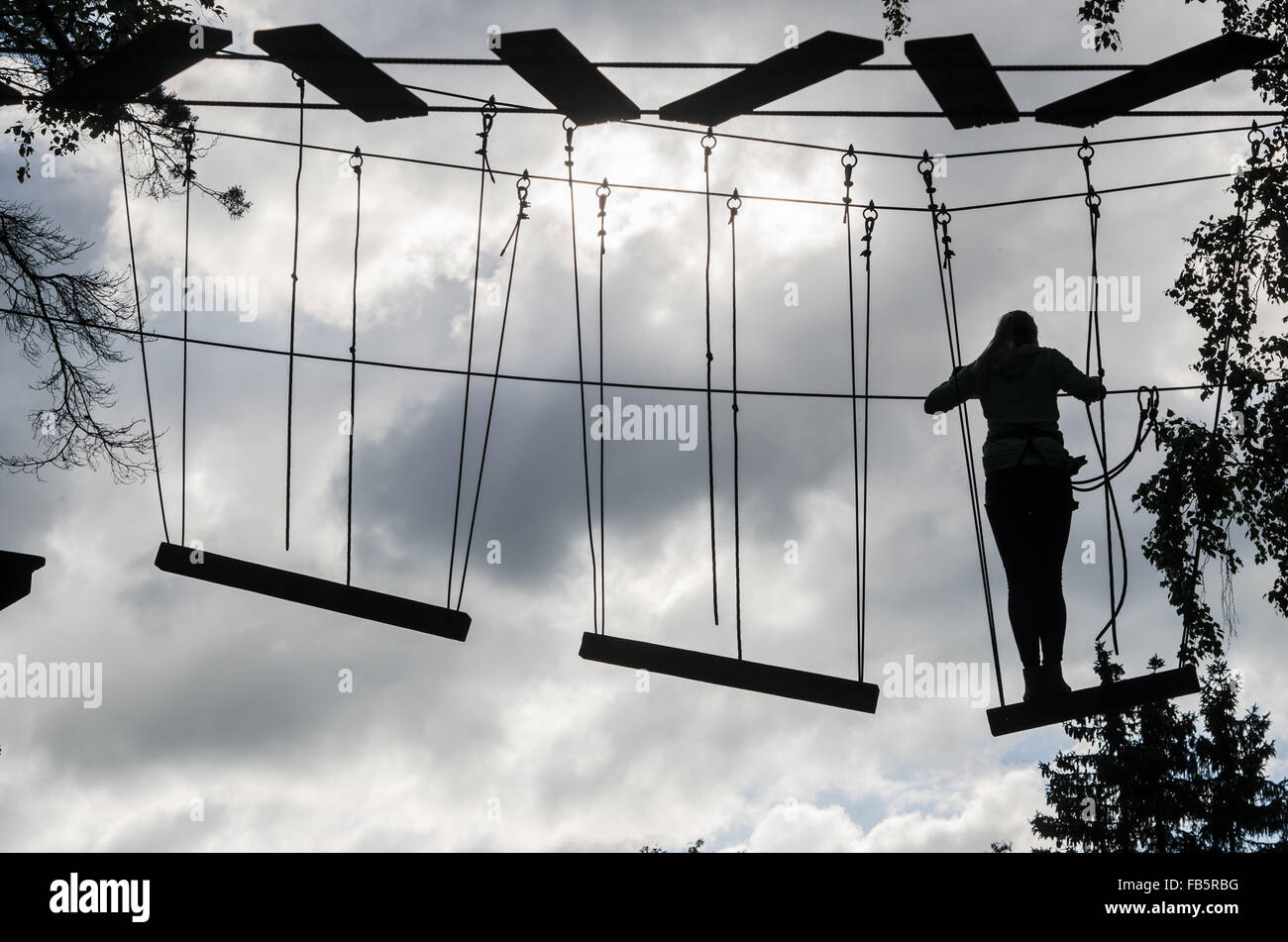 Silhouette of the girl on Dangerous ropeway with tether in rope park Stock Photo