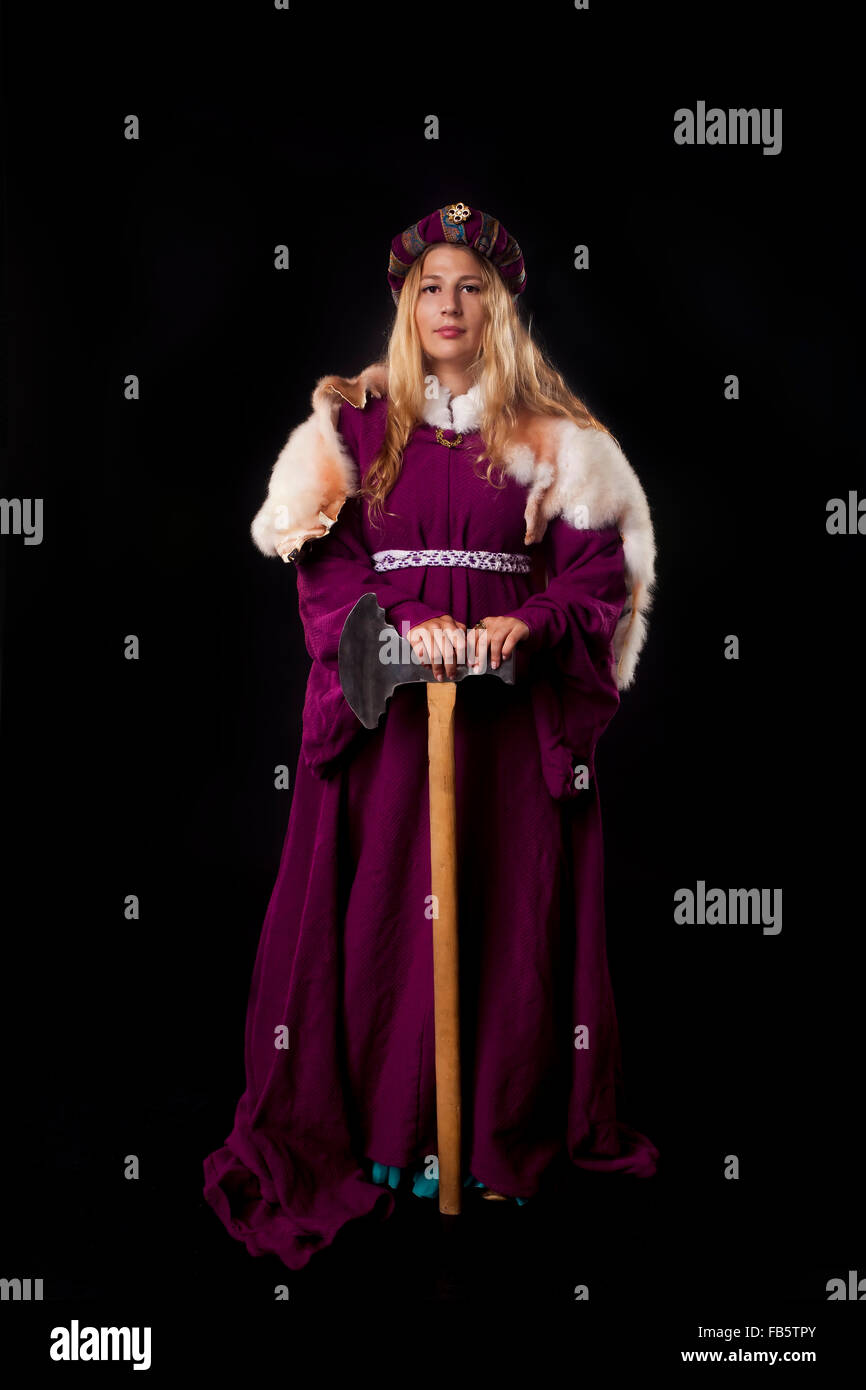 Studio shot of beautiful girl dressed as a medieval noble lady in a mantle leaning on large axe (black background) Stock Photo