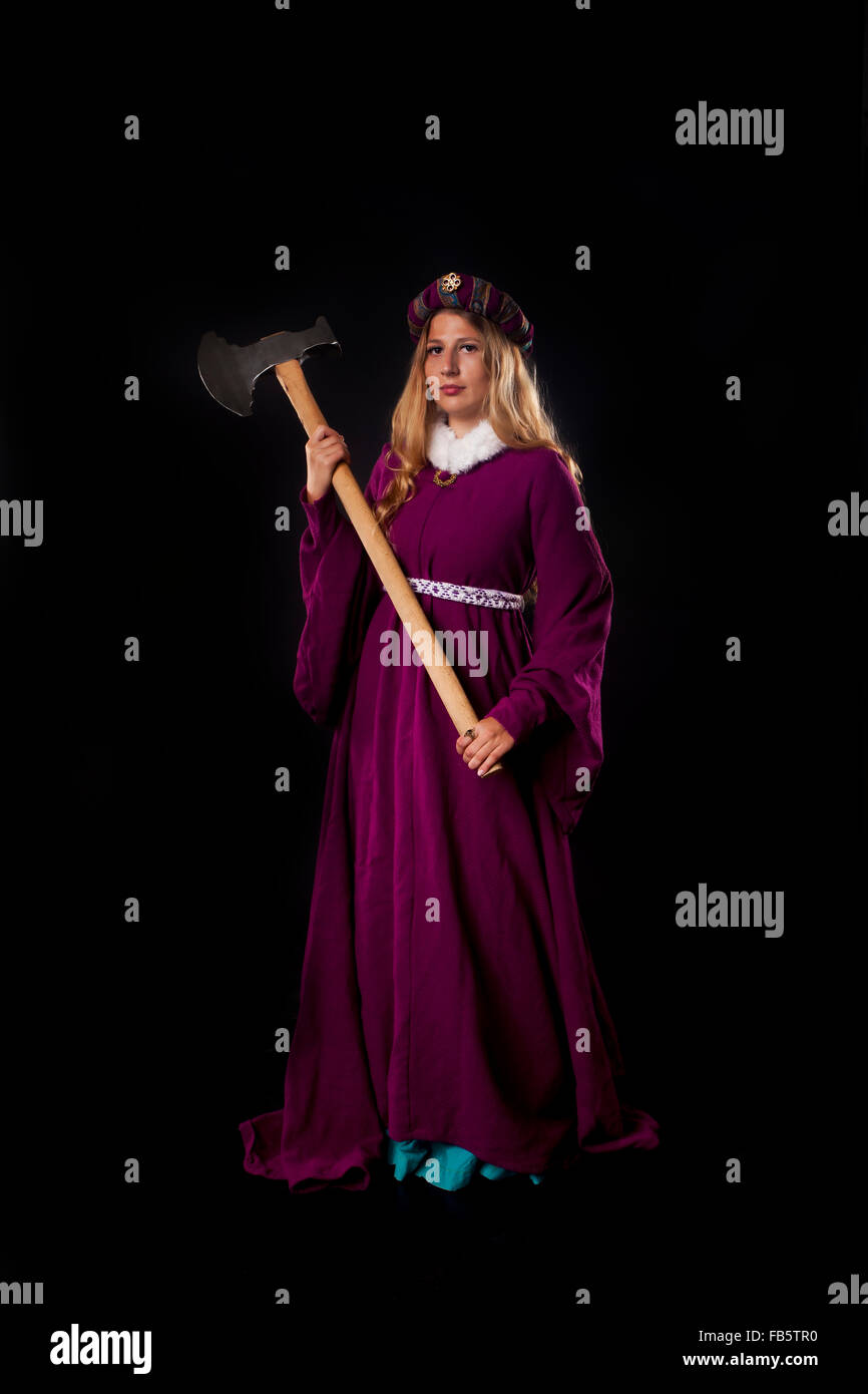 Studio shot of beautiful girl dressed as a medieval noble lady in purple mantle with large axe on black background Stock Photo