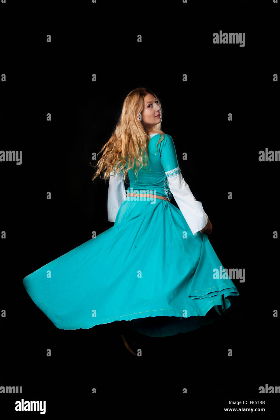 Studio shot of young beautiful girl dancing in a turquoise medieval costume dress (on black background) Stock Photo